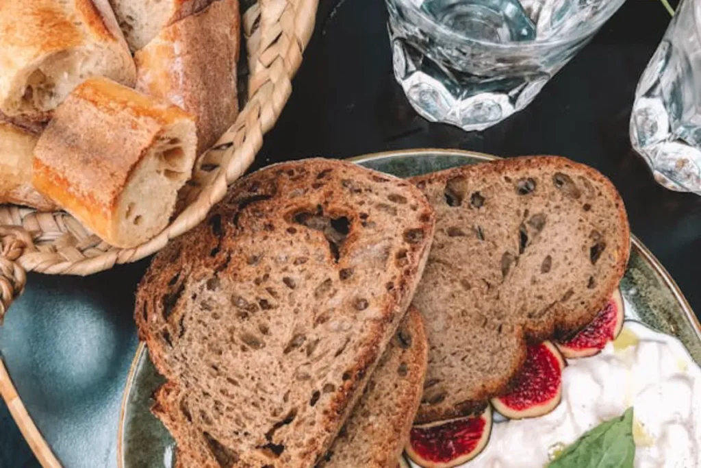 A selection of gluten-free breads including sliced sourdough, multigrain, and white bread on a wooden cutting board.